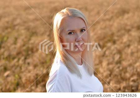 Woman stands in a golden field of wheat during sunset, showcasing natural beauty and serenity in a rural setting 123943626