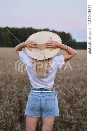 Young woman enjoying a carefree moment in a wheat field near a forest during sunset 123943633