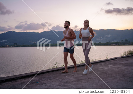 A Couple Jogging Together Alongside the Serene Lake During the Stunning Sunset Hours A Couple Jogging Together Alongside the Serene Lake During the Stunning Sunset Hours 123948594