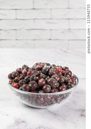 Frozen black currant berries on table in transparent bowl, on light background. Preservation of vegetables and fruits. Natural products Frozen black currant berries on table in transparent bowl, on light background. Preservation of vegetables and fruits. Natural products 123948735