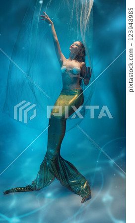 Graceful young woman, mermaid, caught between dreams and reality, extends hand toward light in surreal underwater world. Graceful young woman, mermaid, caught between dreams and reality, extends hand toward light in surreal underwater world. 123948985