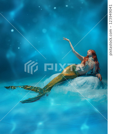 Magical deep-sea redhaired mermaid, siren gazing up, surrounded by floating lights and rippling water. 123949041