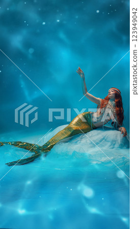 Fantasy mermaid, redhaired woman reaching out with mysterious hand gesture, sparkling tail shimmering in deep blue waters. Mythology Fantasy mermaid, redhaired woman reaching out with mysterious hand gesture, sparkling tail shimmering in deep blue waters. Mythology 123949042