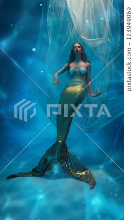 Young woman dressed in mermaid costume, with colorful makeup and seashell bra swimming deep in the ocean against glowing blue background 123949069