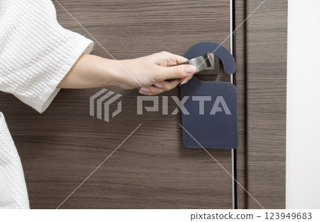 A close-up of a closed wooden door of a hotel room with a mock-up of a black sign and a female hand. 123949683