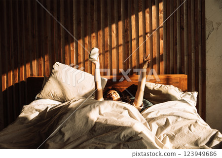 Charming mixed-race teenager laughs and holds cup while lying in bed. Cute African girl is enjoying sunny morning. Charming mixed-race teenager laughs and holds cup while lying in bed. Cute African girl is enjoying sunny morning. 123949686