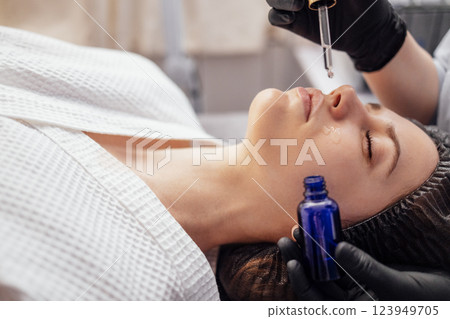 Beautician applies serum from pipette in gloves to the face of client in spa salon Beautician applies serum from pipette in gloves to the face of client in spa salon 123949705