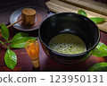 matcha green tea and leaf in black bowl chawan decorated  Chasen, a bamboo matcha whisk, mat over wooden table, concept  of Japanese tea ceremony 123950131