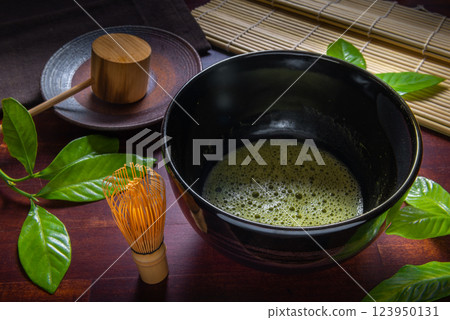 matcha green tea and leaf in black bowl chawan decorated  Chasen, a bamboo matcha whisk, mat over wooden table, concept  of Japanese tea ceremony 123950131