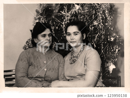 Retro photograph of mother and adult daughter near New Year tree. USSR, 1971. 123950138