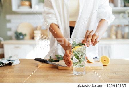 Close-up of a female hands and a glass of lemonade with mint leaves. A young woman prepares a delicious ice drink with a slice of lemon. 123950185