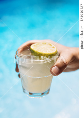 Young male hand holds a glass of a chilled drink with ice cubes. 123950187