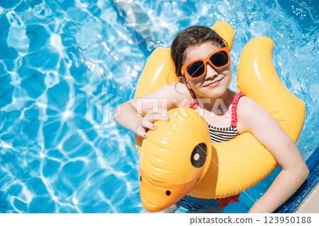 A little girl with an inflatable circle in the shape of a duck jumps into the pool. 123950188