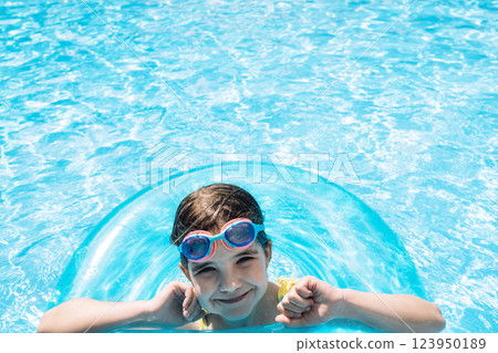 A little girl with an inflatable circle jumped into the pool. A cute kid in a swimsuit A little girl with an inflatable circle jumped into the pool. A cute kid in a swimsuit 123950189