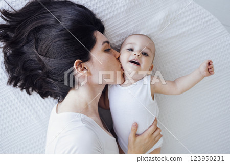 Pretty infant in a white bodysuit with his mom on a light background. Motherhood concept. Pretty infant in a white bodysuit with his mom on a light background. Motherhood concept. 123950231