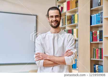 Portrait of young confident man with crossed arms posing inside library office 123950906