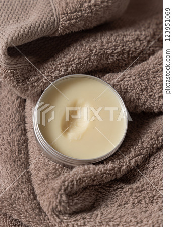 Opened body butter jar on light brown bath towel close up, herbal cosmetics for bodycare 123951069