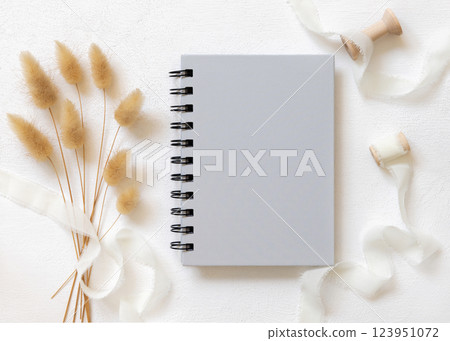 Blank spiral notebook on white plate near silk ribbons and hare's tail grass top view, mockup Blank spiral notebook on white plate near silk ribbons and hare's tail grass top view, mockup 123951072