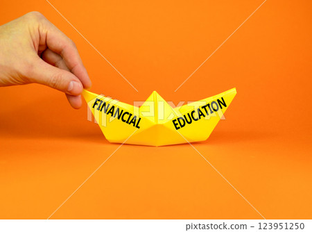 Financial education symbol. Concept words Financial education on beautiful yellow paper boat. Beautiful orange paper background. Businessman hand. Business Financial education concept. Copy space. Financial education symbol. Concept words Financial education on beautiful yellow paper boat. Beautiful orange paper background. Businessman hand. Business Financial education concept. Copy space. 123951250