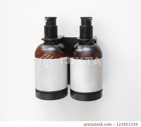 Two amber plastic bottles containing shampoo and conditioner hanging on wall Two amber plastic bottles containing shampoo and conditioner hanging on wall 123951339