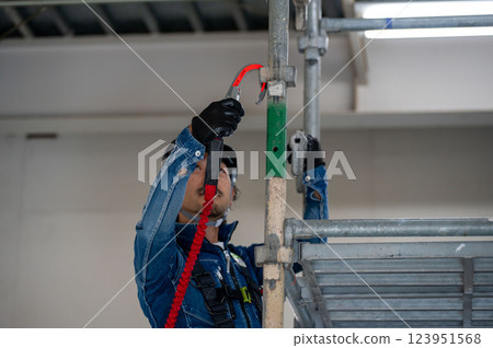 A man in a helmet putting on a safety harness on scaffolding 123951568