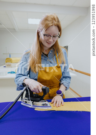 woman strokes a piece of cloth of lady in yellow apron, glasses. female fashion designer woman strokes a piece of cloth of lady in yellow apron, glasses. female fashion designer 123951998