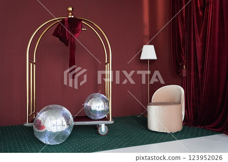 Studio interior with luggage trolley with mirrored disco balls in a New Year's interior, on the background of a red wall with space for copying. High quality photo 123952026