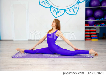 Flexible woman performing a full split yoga pose on a purple mat Flexible woman performing a full split yoga pose on a purple mat 123952029