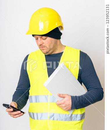 a man in a yellow work vest, yellow safety helmet with papers and a cell phone in his hands. High quality photo a man in a yellow work vest, yellow safety helmet with papers and a cell phone in his hands. High quality photo 123952131