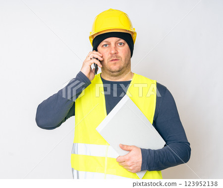 a man in a yellow work vest, yellow safety helmet with papers and a cell phone in his hands. High quality photo a man in a yellow work vest, yellow safety helmet with papers and a cell phone in his hands. High quality photo 123952138