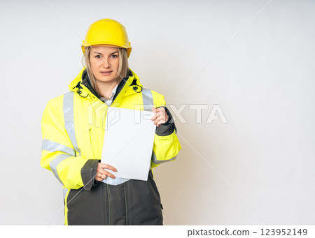 a girl in a yellow special protective jacket and a protective yellow helmet with papers in her hands. High quality photo 123952149