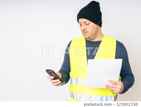 a man in a yellow work vest, with papers and a telephone in his hands. High quality photo a man in a yellow work vest, with papers and a telephone in his hands. High quality photo 123952150