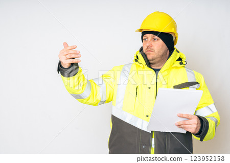 a man in a yellow working winter jacket, yellow safety helmet with papers in his hands. High quality photo a man in a yellow working winter jacket, yellow safety helmet with papers in his hands. High quality photo 123952158
