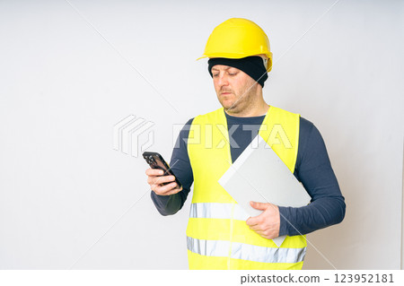 a man in a yellow work vest, yellow safety helmet with papers and a cell phone in his hands. High quality photo a man in a yellow work vest, yellow safety helmet with papers and a cell phone in his hands. High quality photo 123952181