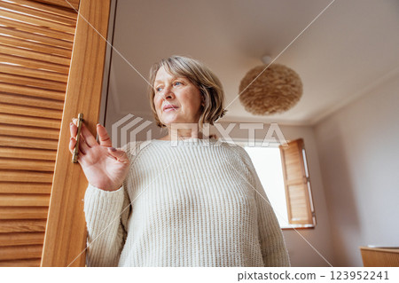 elderly woman in a knitted sweater looks out the apartment window elderly woman in a knitted sweater looks out the apartment window 123952241