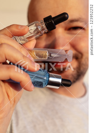 Close-up of a male hand with cosmetic bottles of serums. A young man is smiling and holding beauty products. Glass bottles with moisturizing vitamin essence. Close-up of a male hand with cosmetic bottles of serums. A young man is smiling and holding beauty products. Glass bottles with moisturizing vitamin essence. 123952252