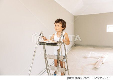 A little boy climbs on a stepladder in a renovated room. A laughing child is playing among the repairs in the house. A little boy climbs on a stepladder in a renovated room. A laughing child is playing among the repairs in the house. 123952258