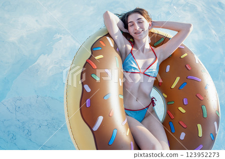 An attractive female teen in a swimsuit has closed her eyes and is lying on an inflatable circle. The girl with braces smiles and enjoys relaxing in the pool. 123952273