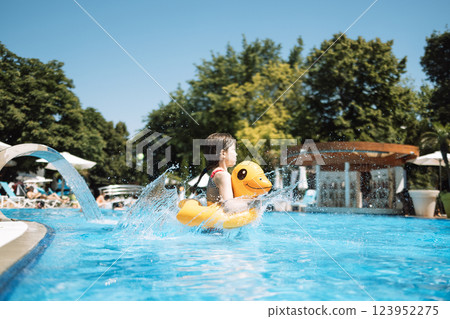 A little girl with an inflatable circle in the shape of a duck jumps into the pool. 123952275
