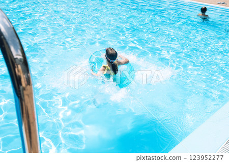 A little girl with an inflatable circle jumped into the pool. A cute kid in a swimsuit 123952277