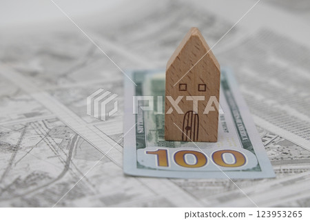 A wooden model house stands on a dollar bill against the background of a land plot scheme, 123953265