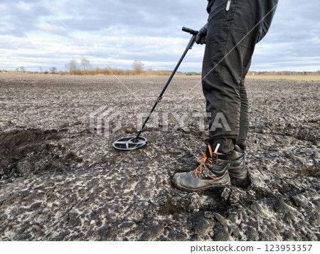 Treasure hunter searches for ancient coins in the ground using a metal detector. Man with a metal detector in a field in search of treasure. Treasure hunter searches for ancient coins in the ground using a metal detector. Man with a metal detector in a field in search of treasure. 123953357