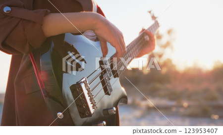 Girl Plays Bass Music Instrument On The Beach At Sunset Near Ocean Girl Plays Bass Music Instrument On The Beach At Sunset Near Ocean 123953407