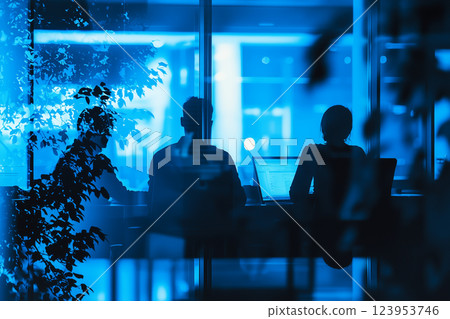 Team members collaborating late at night in a modern office with a layered view of blue lighting and reflections 123953746