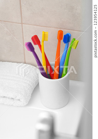 Multicolored toothbrushes. Six bright toothbrushes in a white glass in the bathroom next to a white washcloth. Rainbow. Place for text. Ritual. Oral hygiene. Multicolored toothbrushes. Six bright toothbrushes in a white glass in the bathroom next to a white washcloth. Rainbow. Place for text. Ritual. Oral hygiene. 123954125