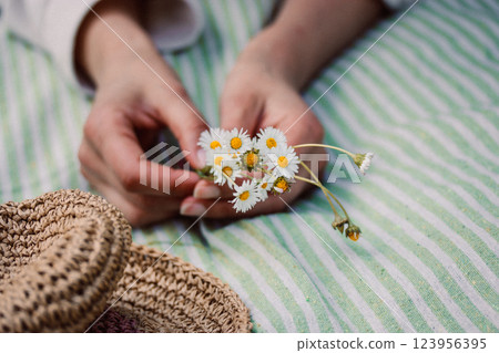 A bouquet of field white daisies plucked in a spring meadow. A young woman lying on a striped plaid with a bouquet of wildflowers. Straw female sunhat 123956395