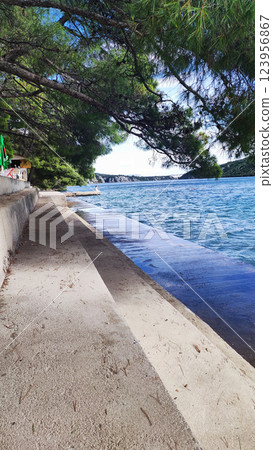 A tranquil shoreline is visible, with clear blue waters lapping against the sandy bank. Lush green trees line the area, providing shade and enhancing the peaceful atmosphere. 123956867
