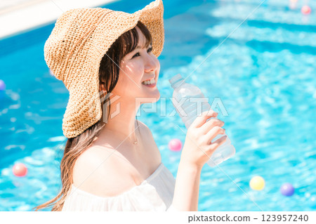 戴草帽的年輕女子在泳池邊喝礦泉水 123957240