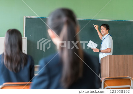 A male teacher giving a lesson in front of a blackboard and students taking a lesson 123958192