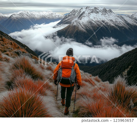 A hiker wearing a winter jacket and hat, trekking up a misty mountain trail in the early morning. 123963657